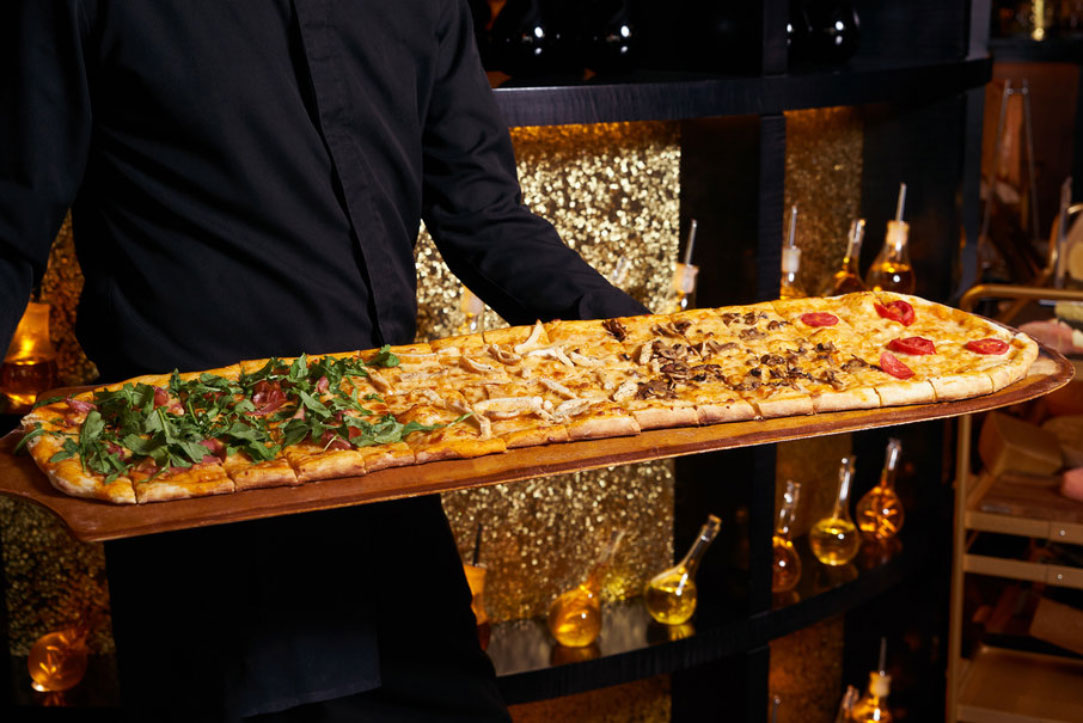 Meterpizza mit verschiedenen Belägen auf einem langen Holzbrett bei Pizza Picco XXL